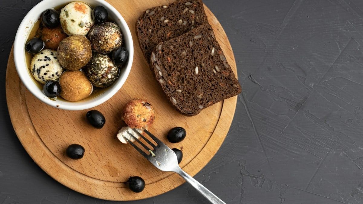 spicy cheese balls in butter next to a fork and bread on a curved cutting board